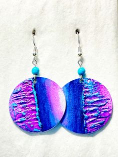 two circular earrings with blue and purple designs on them, hanging from silver earwires