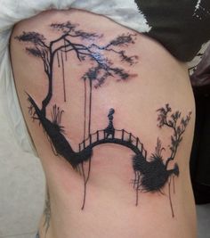 a woman with a tattoo on her back is standing in front of a tree and bridge