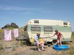 two people sitting in chairs next to an old camper and washing clothes on a line