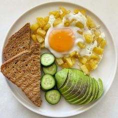 a white plate topped with an egg, toast and sliced cucumber next to slices of bread