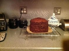 a chocolate cake sitting on top of a cooling rack next to coffee pots and other items