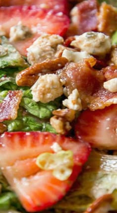 a salad with strawberries, bacon, and other toppings is shown in close up