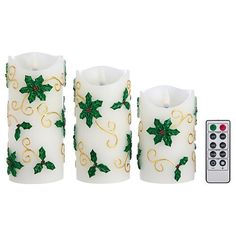 three white candles with green holly decorations next to a remote control on a white background