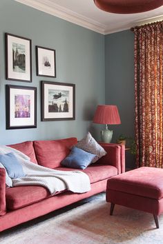 a living room with red couches and pictures on the wall above them, along with a footstool