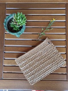 a small potted plant sitting on top of a wooden table next to a crochet purse