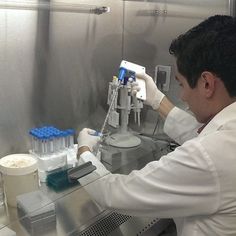 a man in white lab coat and gloves working on some bottles with blue caps around them