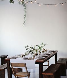 a dining table set with place settings and lights strung from the ceiling, along with wooden chairs