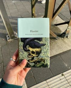 a person holding up a book with a skull on it's cover in front of a bench