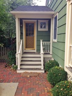 a small house with steps leading up to the front door and side porch that is painted green