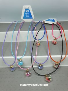 four necklaces with different colors and designs hanging from the side of a shelf in a store