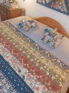 a bed covered in lots of different types of quilts and pillows on it's headboard