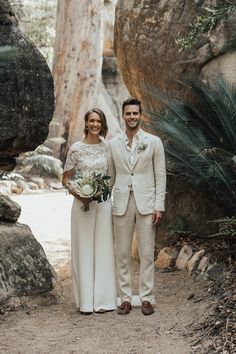 a man and woman standing next to each other in front of some large rocks with trees