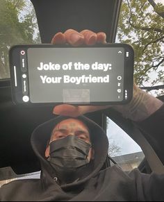 a man wearing a face mask holding up a cell phone with the message joke of the day your boyfriend