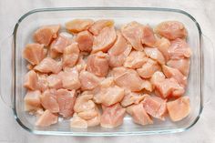 raw chicken pieces in a glass dish on a white tableclothed surface, ready to be cooked