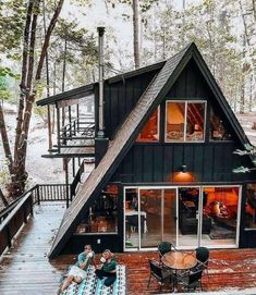 two people sitting on a picnic blanket in front of a black cabin with stairs leading to the upper floor