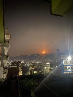 the city lights shine brightly in the dark night sky over some buildings and hills behind them