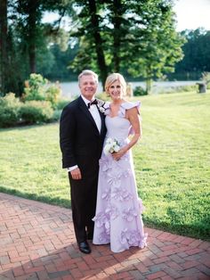 a man and woman standing next to each other on a brick walkway in front of trees