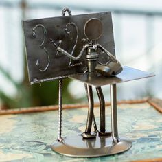 a metal figurine holding a piece of art on top of a wooden table