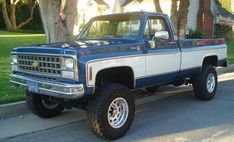 a blue and white pick up truck parked on the side of a road next to a house