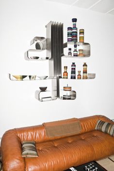 a brown leather couch sitting in front of a wall mounted shelf with bottles on it