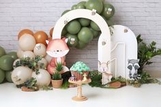 a table topped with lots of balloons and animals next to a cake stand filled with cupcakes