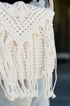 a white crocheted bag with tassels hanging from it's side