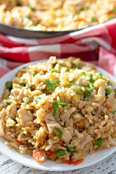 a white plate topped with rice covered in chicken and veggies next to a skillet