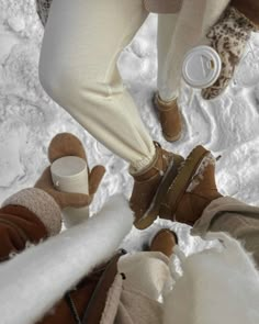 two people standing in the snow with their feet up and one person holding a coffee cup