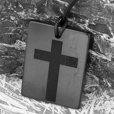 a black and white photo of a cross on a sign hanging from a rope in front of a stone wall