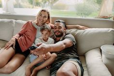 a man, woman and child sitting on a couch with a remote control in their hands