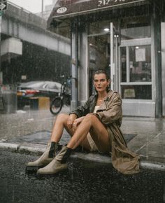 a woman is sitting on the curb in the rain