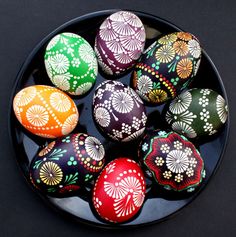 colorful painted eggs in a bowl on a black tablecloth with white and green designs