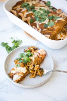 a white plate topped with a slice of enchilada next to a casserole dish