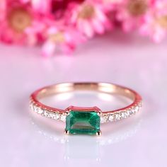 an emerald and diamond ring with pink flowers in the background