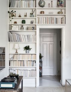 a living room filled with lots of white bookshelves next to a table and chair