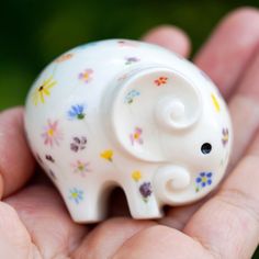 a small white elephant figurine sitting in someone's hand with flowers all over it