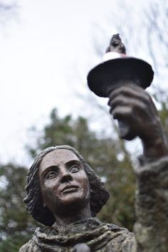 a statue holding a lamp in the air with trees in the back ground behind it