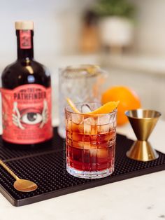 an alcoholic drink on a tray next to a bottle and two glasses with orange peels