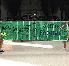 two people holding a banner that says are you going to some football?