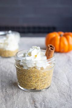 two small glass jars filled with food on top of a wooden table next to an orange pumpkin