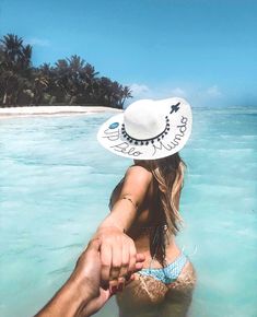 a man and woman holding hands while standing in shallow water near an island with palm trees