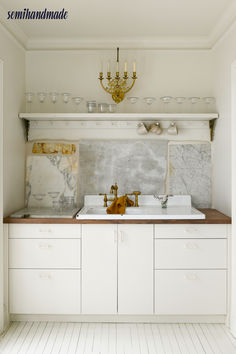 a kitchen with white cabinets and marble counter tops, chandelier above the sink