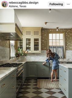 a woman standing in a kitchen next to a stove top oven and countertop with drawers