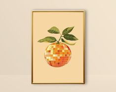 an orange with green leaves on it is shown in a gold frame against a beige wall