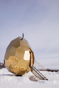 a large golden object sitting on top of snow covered ground next to a stair case