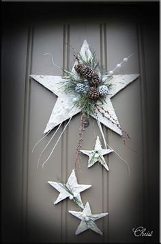 a white star hanging from the side of a door with pine cones and evergreen needles