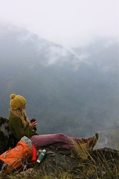 a woman sitting on top of a mountain while looking at her cell phone