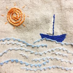 an embroidered sailboat on a piece of cloth next to a small orange and white flower