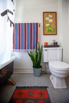 a white toilet sitting next to a bath tub in a bathroom under a painting on the wall