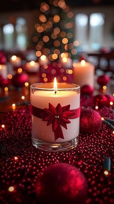 a lit candle with a red bow on it sitting in front of some christmas ornaments